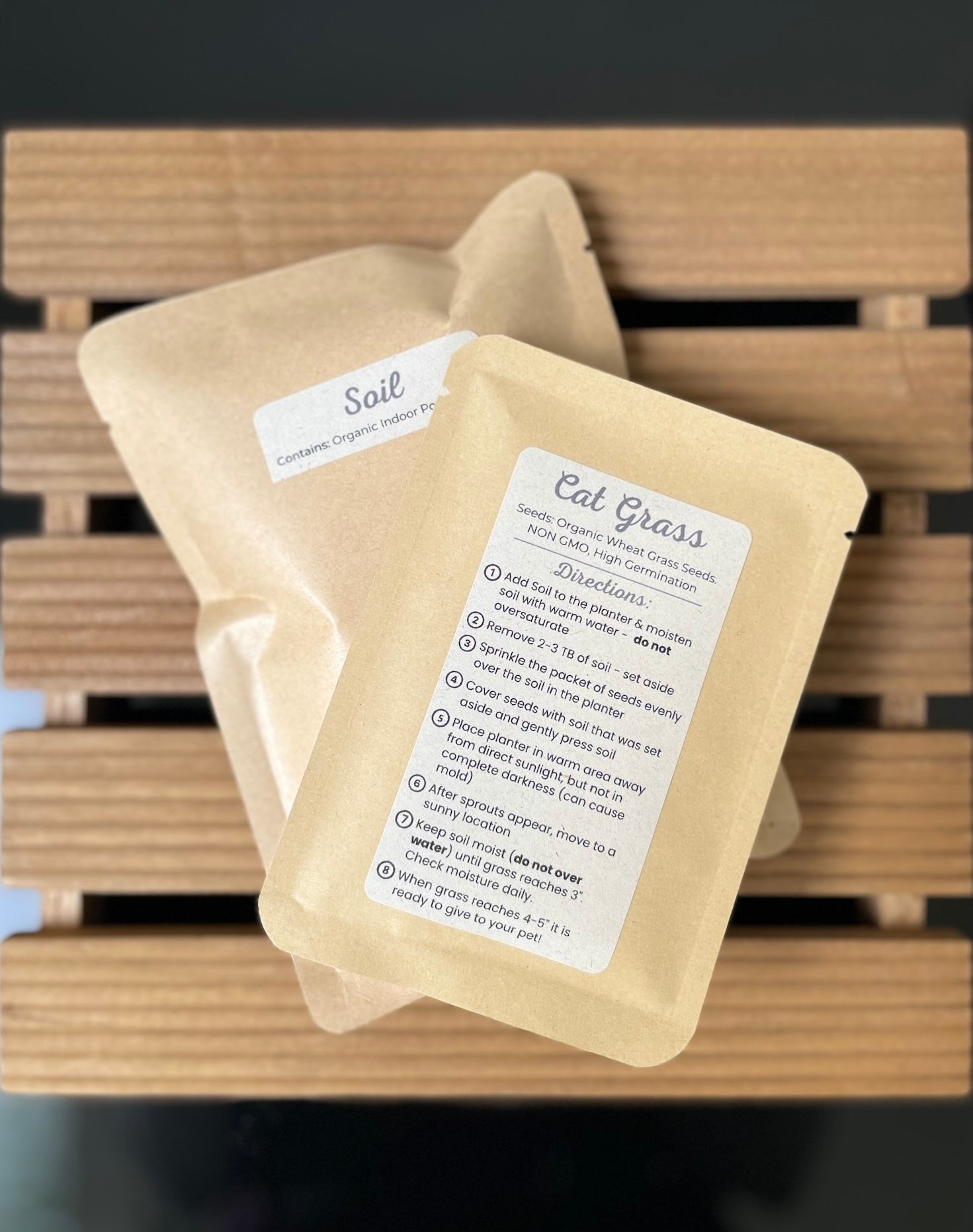 One package of cat grass and one package with planting soil on a wooden surface with labels.