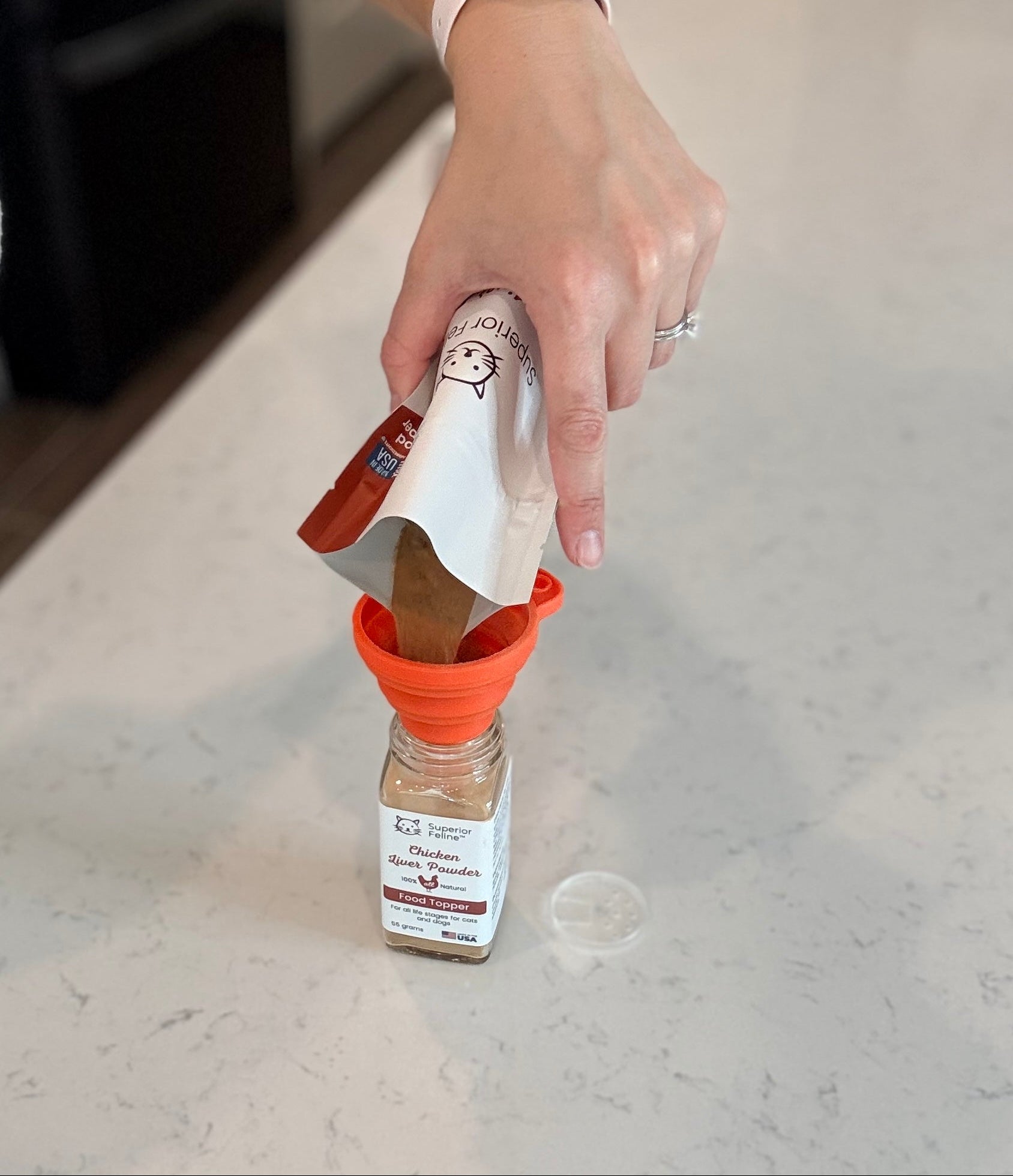 Person pouring Liver Powder Food Topper into a shaker jar using an orange silicone funnel