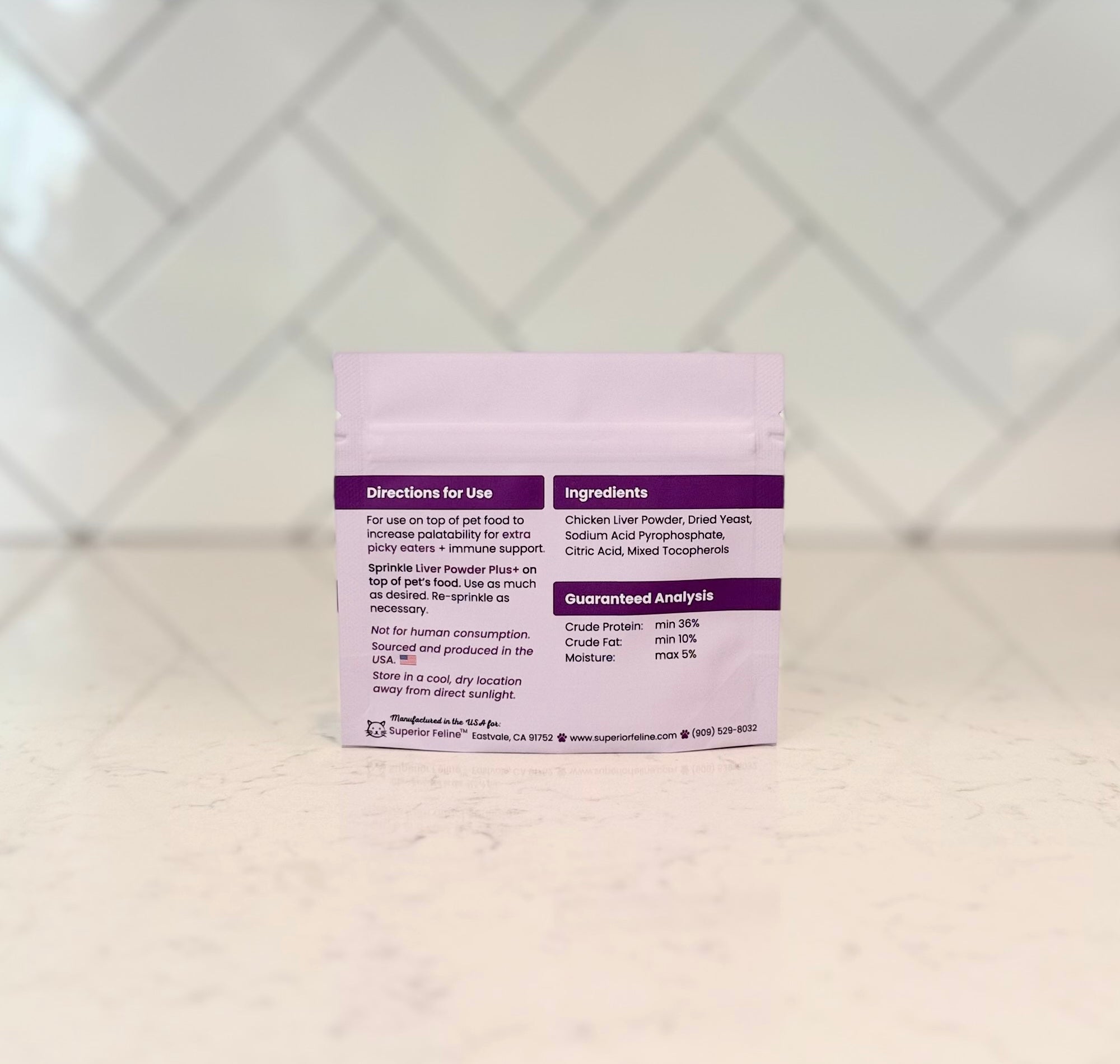 Back side of Superior Feline trial size liver powder plus package with text about directions and ingredients on a countertop with a tiled backsplash