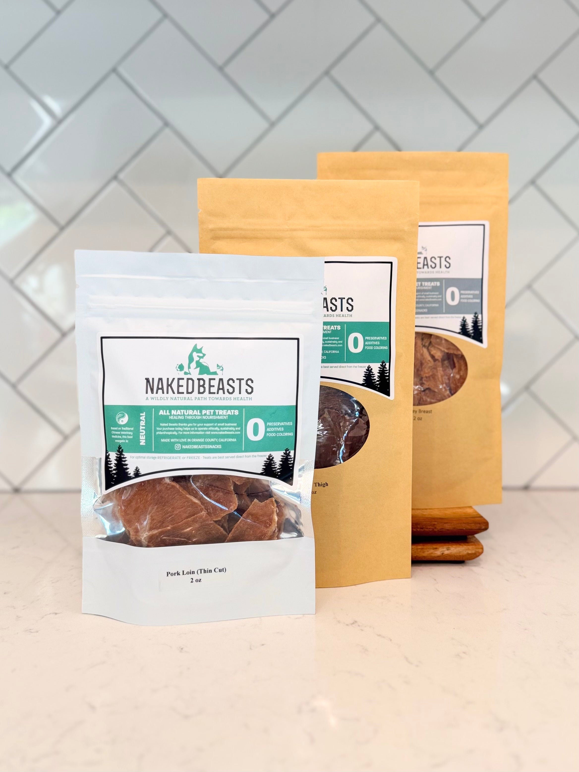 Naked Beasts pet treat packages on a kitchen counter with a tiled wall background