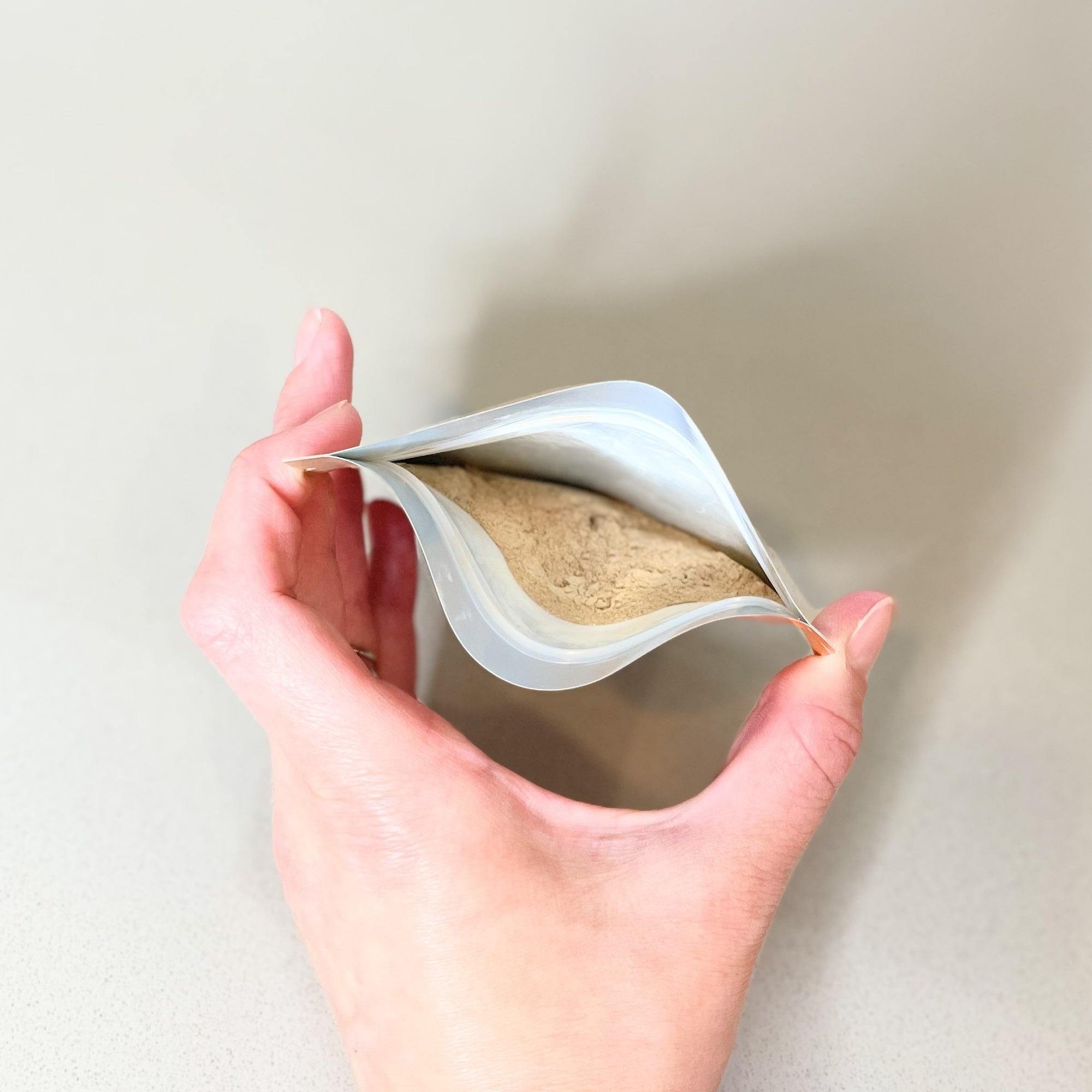Hand holding a plastic pouch showing the powdered contents of the Trial Size Original Formula Homemade Cat Food Supplement Mix