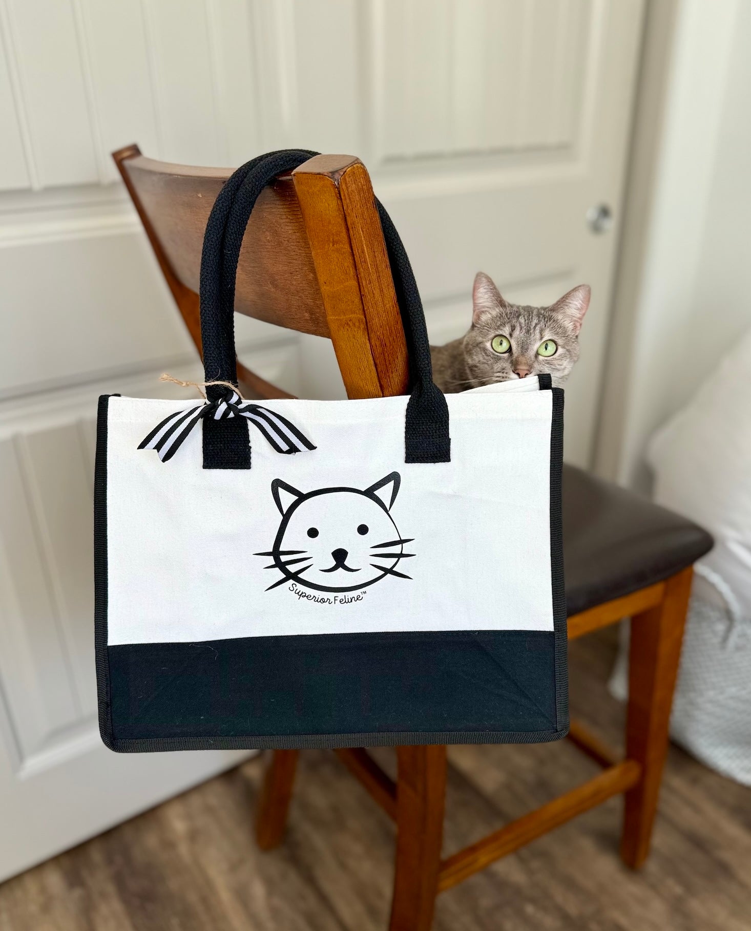 Superior Feline branded tote bag hanging on a chair with a cat peeking out from behind.