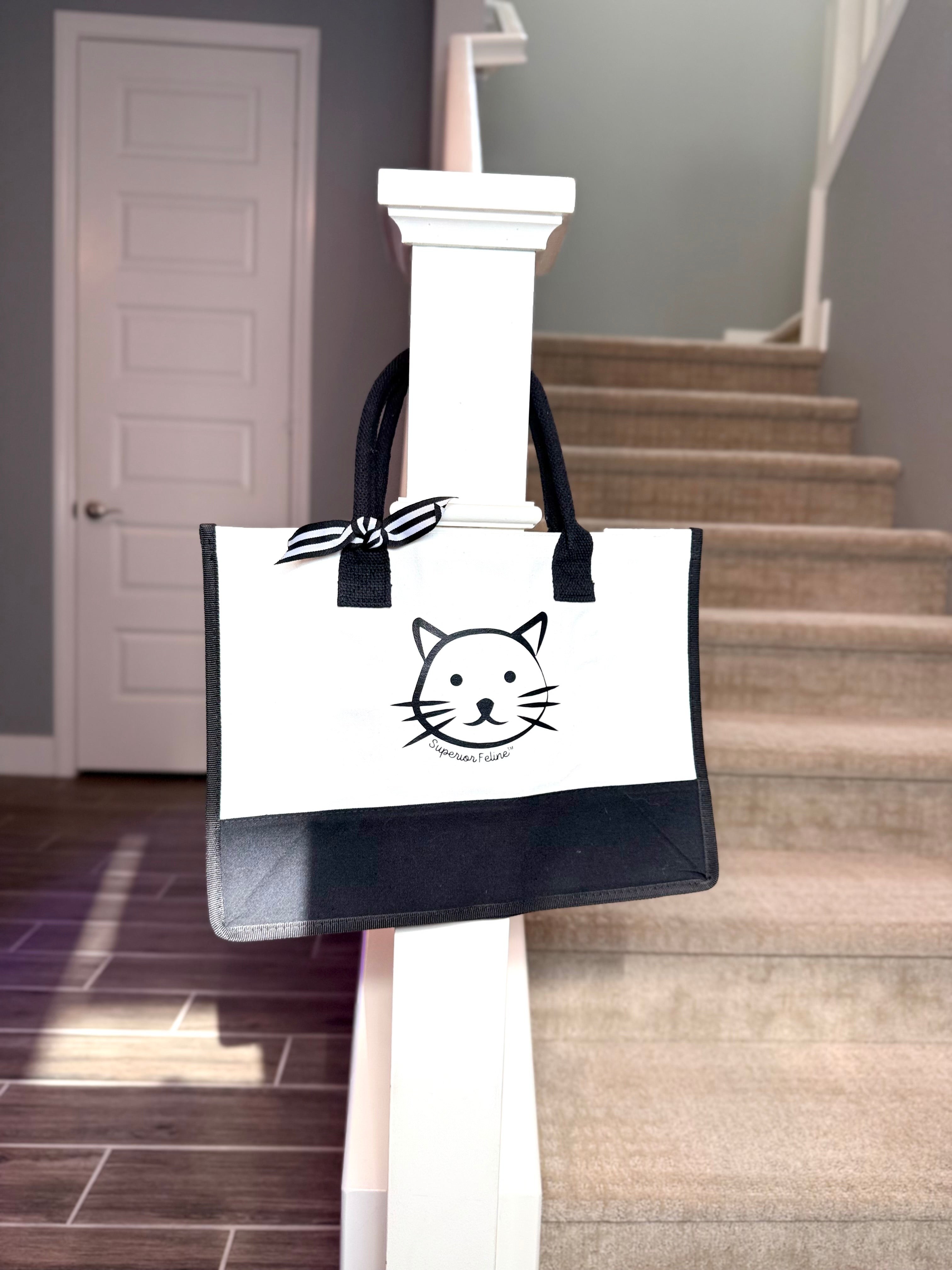 Tote bag featuring the Superior Feline cat design hanging on a white column in a room with stairs.